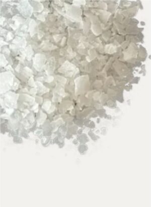 A close-up view of translucent, crystalline magnesium chloride flakes piled against a white background.